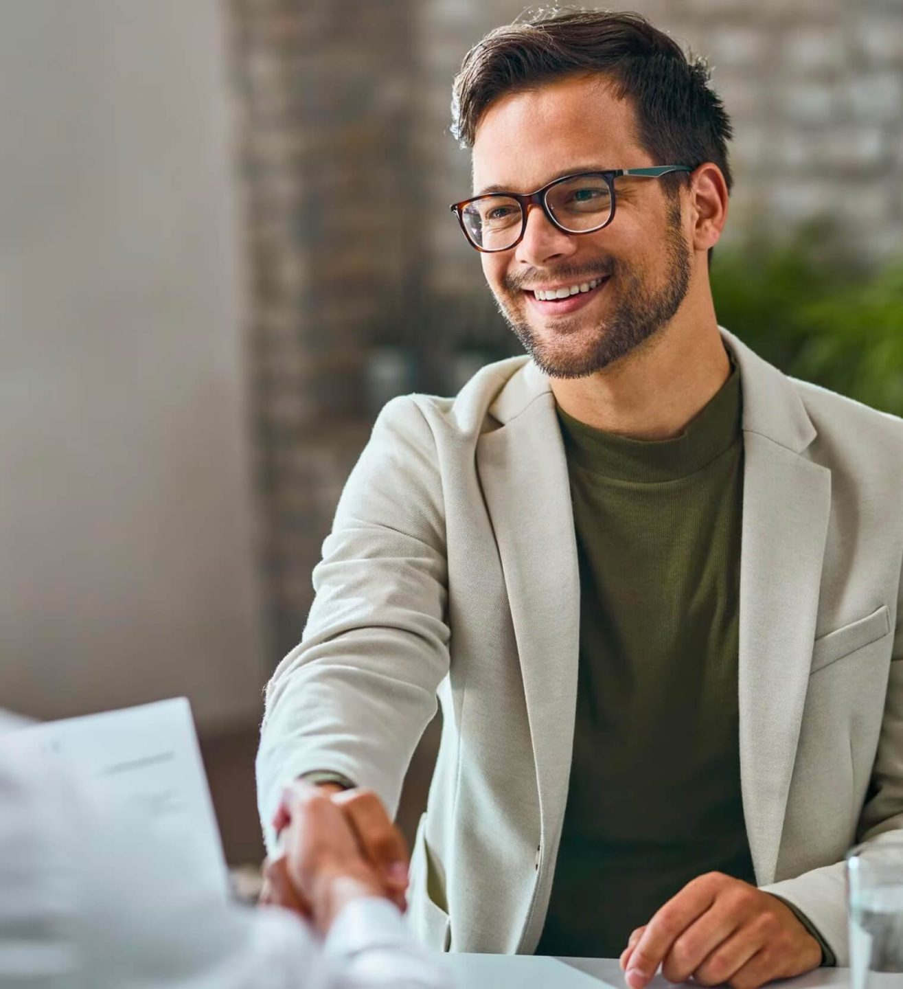 Jeune homme en lunettes et en blazer serrant la main de quelqu'un