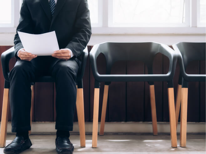 Un candidat masculin pour un emploi attend dans une salle d'attente portant un costume et tenant son curriculum vitae.