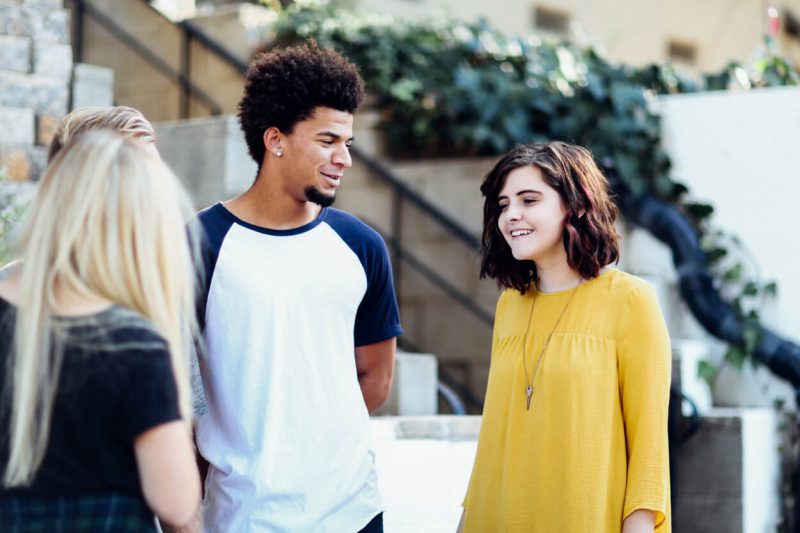 Un groupe de jeunes : une jeune femme caucasienne, un jeune homme noir et une jeune femme blonde en conversation